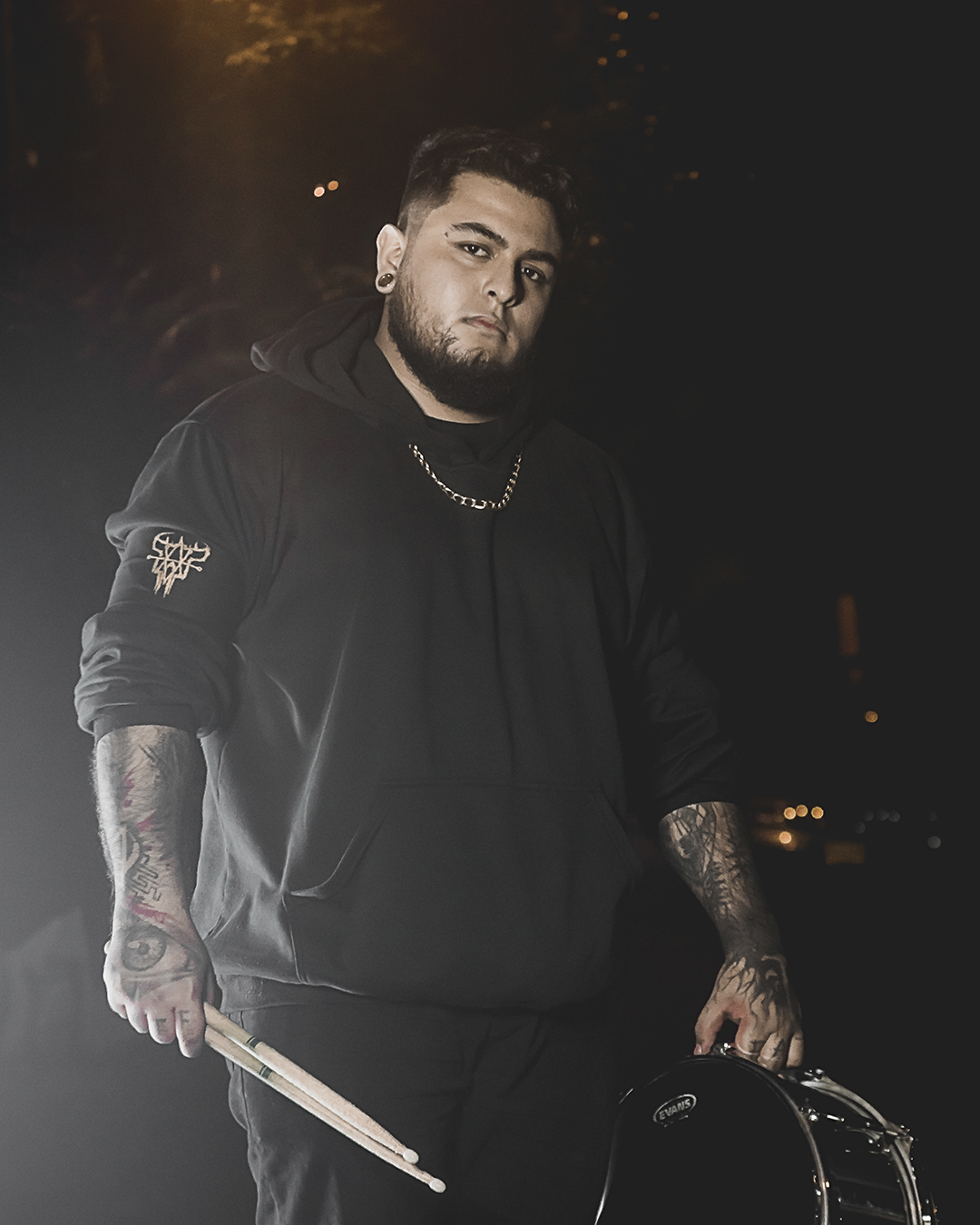 Foto de baterista de la banda ground of chaos sostienendo un redoblante y unas baquetas en la noche con ropa negra